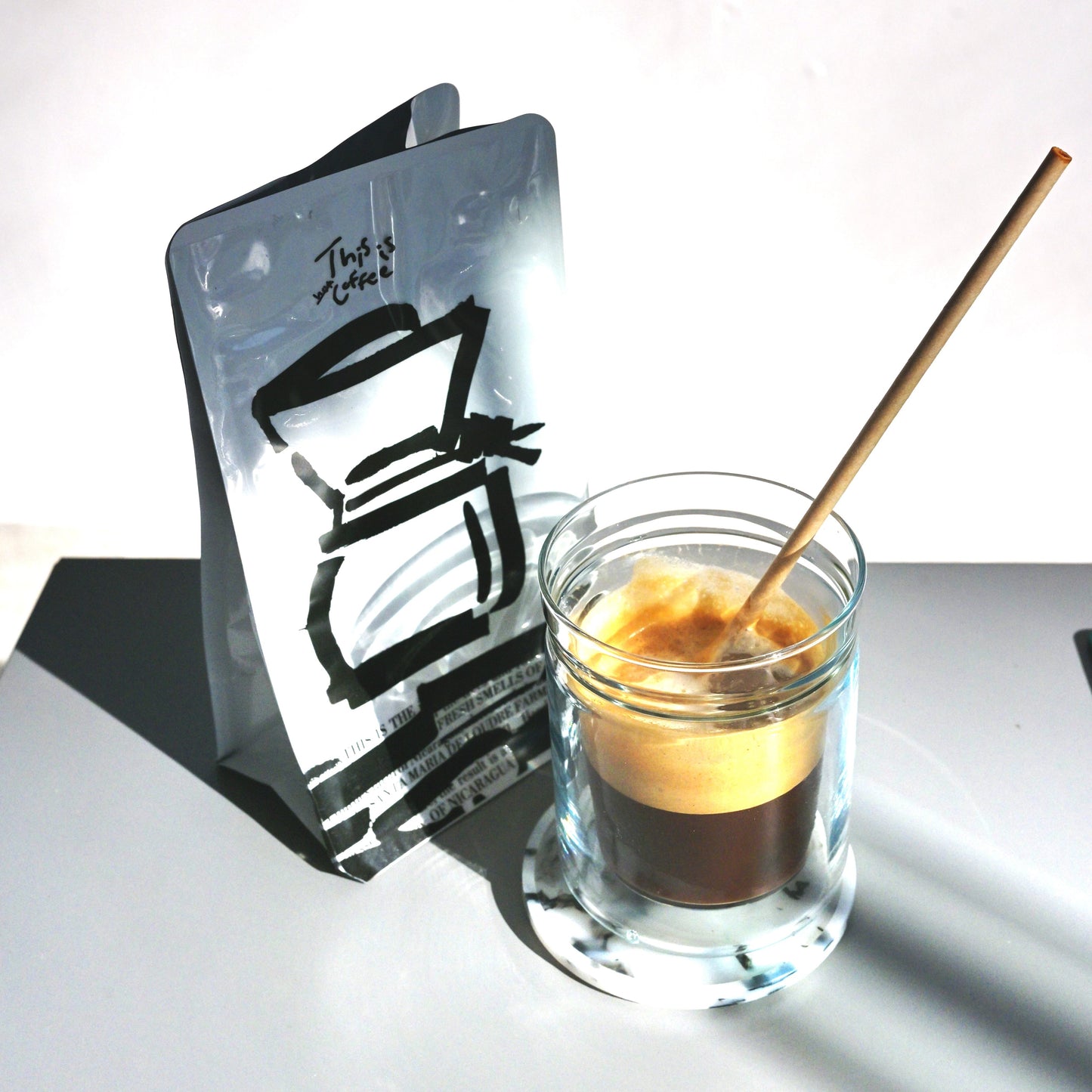 Glass with a shot of coffee and a wooden stirrer next to a black and white illustration on a white background
