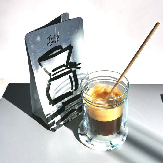 Glass with a shot of coffee and a wooden stirrer next to a black and white illustration on a white background
